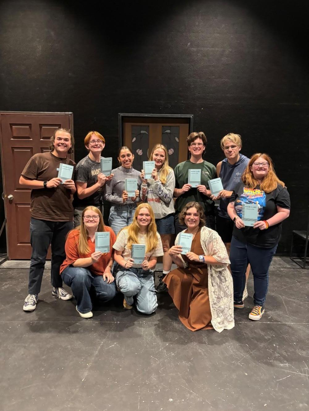 A group of cast members hold script books.