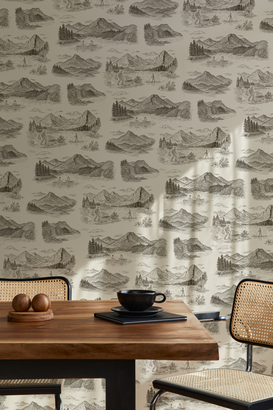 A vignette with a dining table and chairs with a dark brown and white wallpaper behind it
featuring images of mountains, pine trees, and lakes.