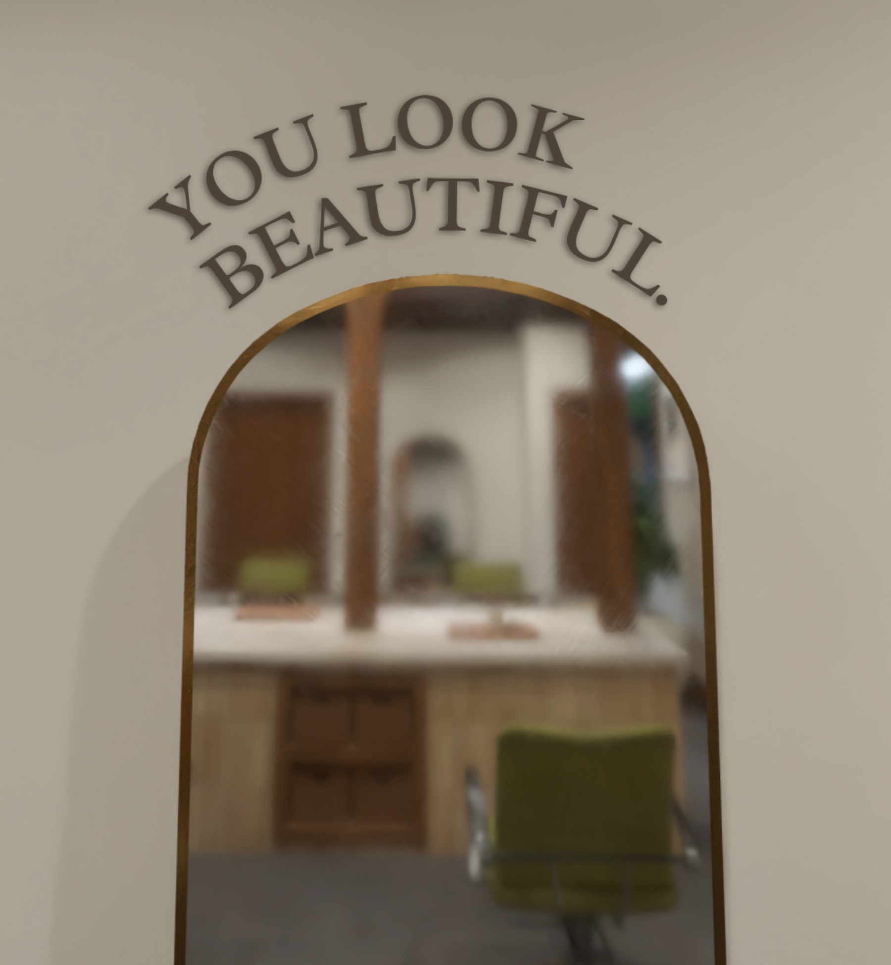 A close-up shot of an arched, gold-trimmed mirror in a salon with the words "YOU LOOK BEAUTIFUL." arched in elegant lettering above it. The mirror's reflection shows a soft-focus view of the salon interior, including wood-paneled stations and olive-green chairs.