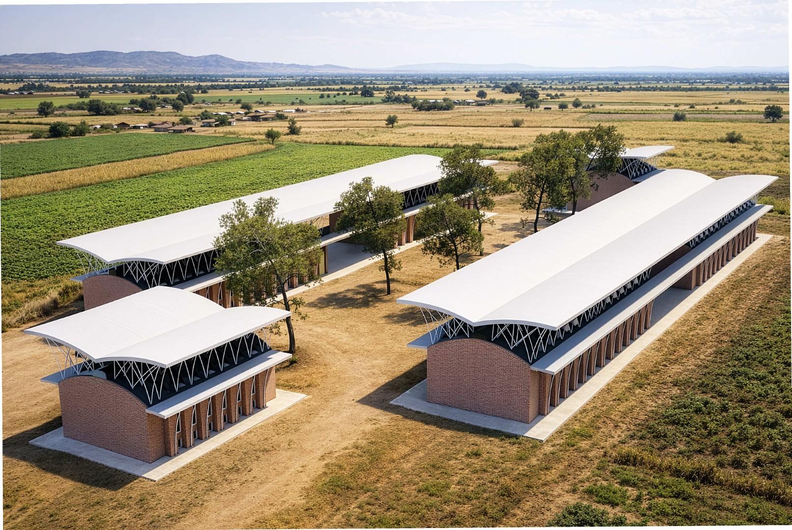 Aerial view of multiple brick buildings with curved roofs and large canopy structures
arranged around a central courtyard in a rural landscape.