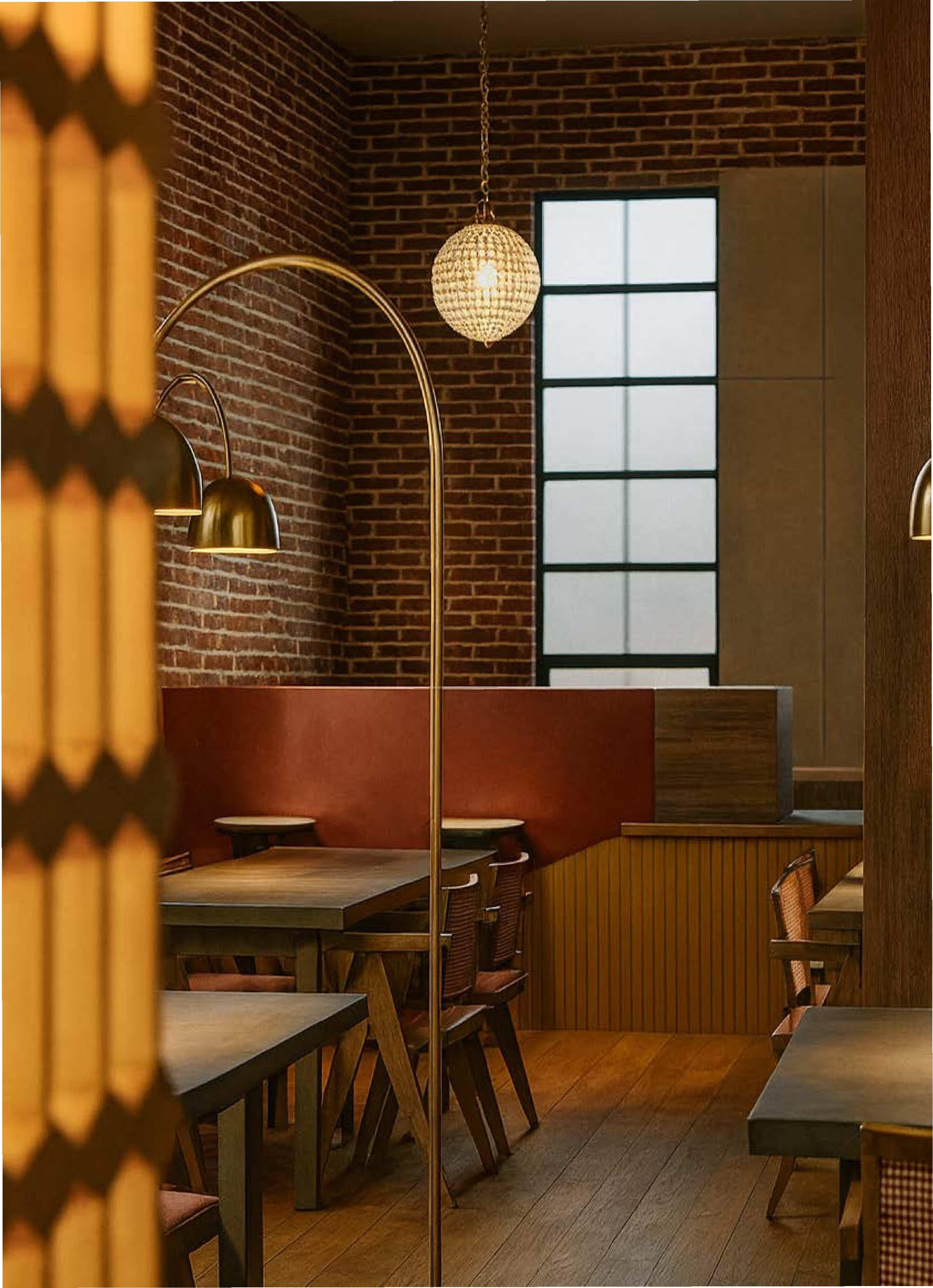 Warm-toned interior with brick walls, wood finishes, and booth seating, featuring pendant
lighting and a tall window.