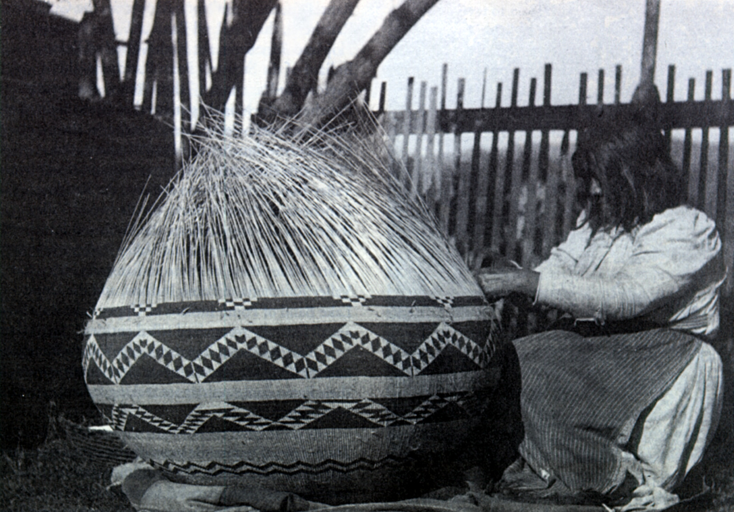 A large woven basket being worked on by a woman.